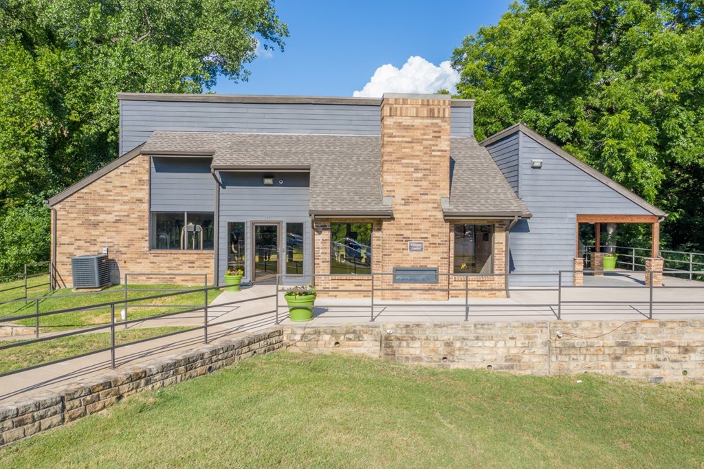 An apartment building with a grey roof and a stone wall in front at Vine Apartments in Arlington, TX