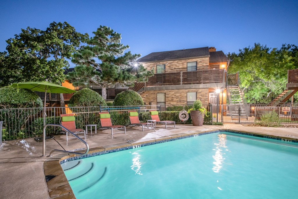 A pool surrounded by trees and chairs in front of a house at Vine Apartments in Arlington, TX