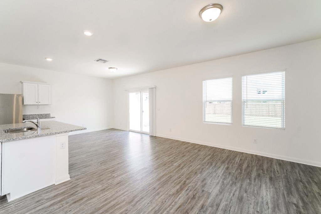 an empty living room with a kitchen in the background