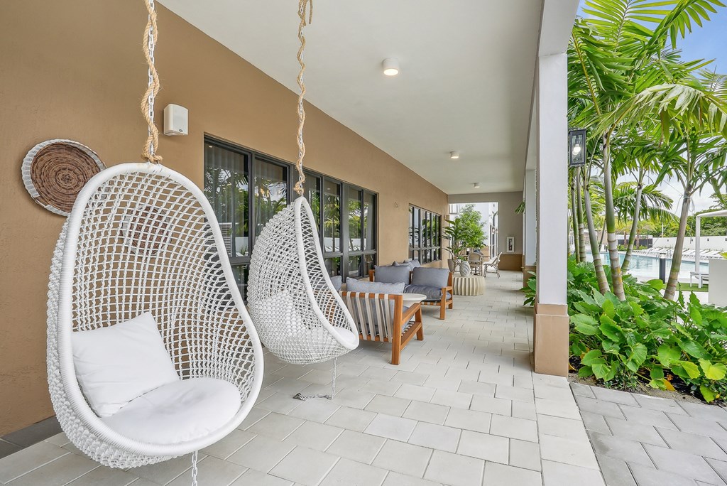 a seating area with hanging chairs and a pool in the background at Westgate on Univeristy in Lauderhill, FL