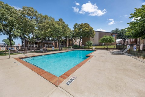 A large outdoor swimming pool surrounded by trees and a building in the background.