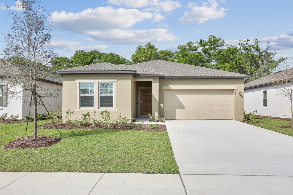 a home with a concrete driveway and a tree in the front yard at Beacon at Woodland Village, Florida