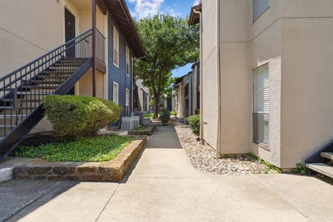 A yellow apartment building exterior and paved walkway at Windridge on the Parkway in Dallas, TX