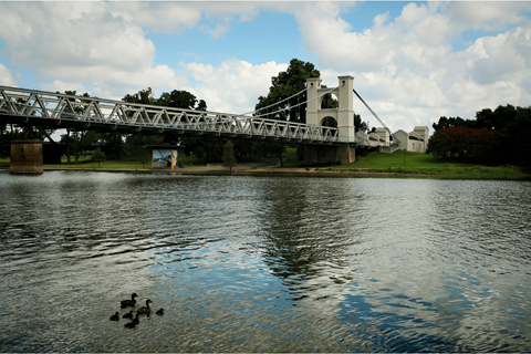 A bridge over a body of water with ducks swimming in the foreground.