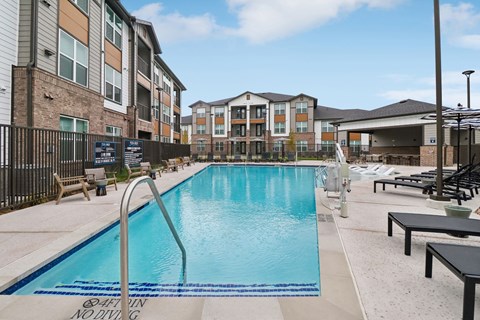A swimming pool with lounge chairs and umbrellas is surrounded by apartment buildings at Whispering Pines in Euless, TX
