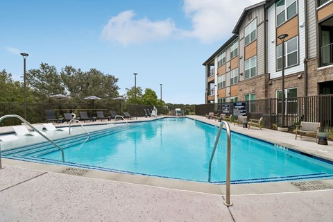 A fenced swimming pool with umbrellas and lounge chairs at Whispering Pines in Euless, TX