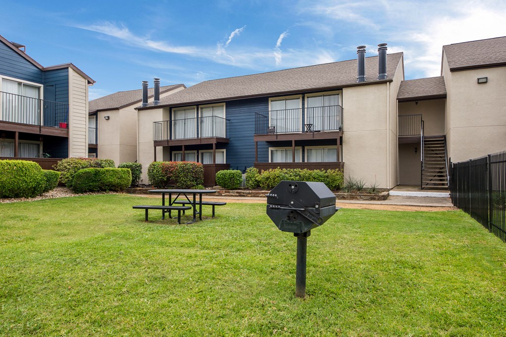 a yard with a picnic table in front of an apartment building