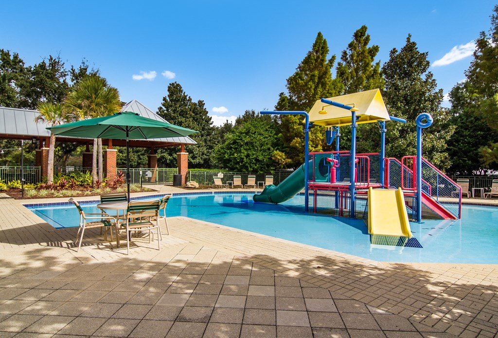 a swimming pool with a playground and tables and chairs