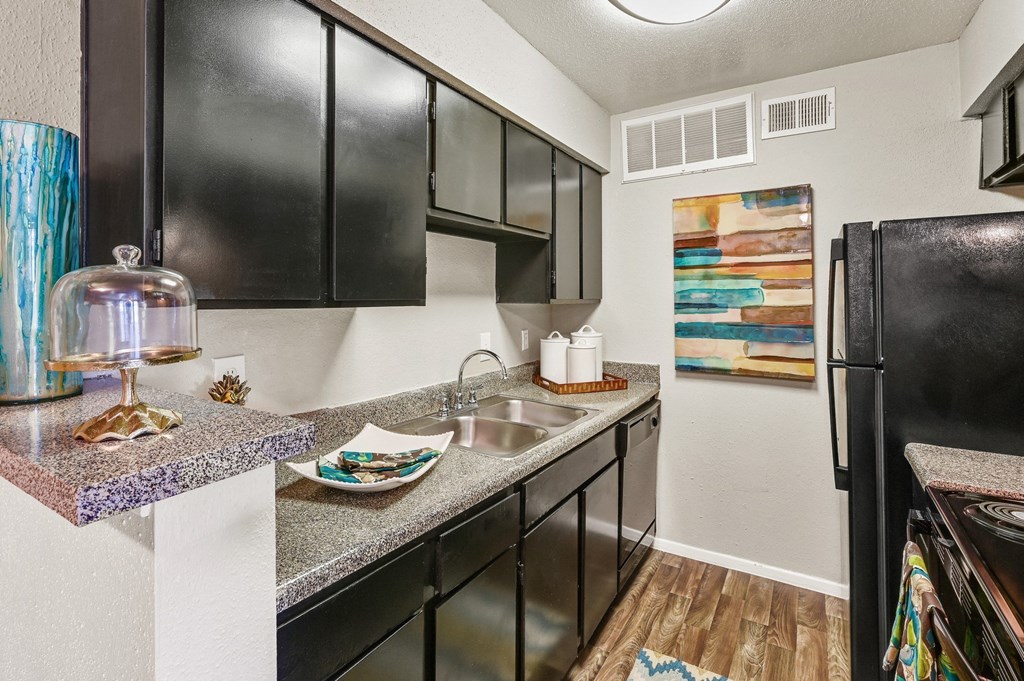 a kitchen with black cabinets, sink and fridge at Bear Creek Crossing apartments in Houston, TX