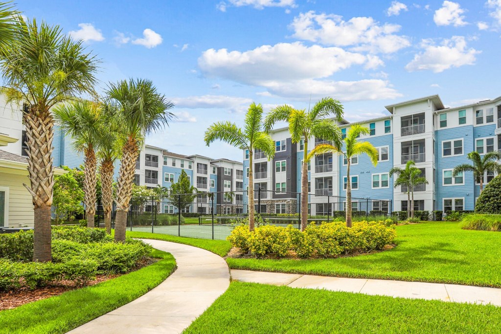 Sidewalk surrounded by luscious green landscape and palm trees at Dunedin Commons apartments in Dunedin, FL