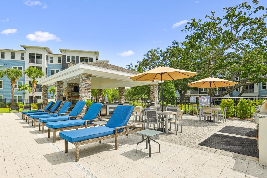 Poolside lounge chairs and umbrellas at Dunedin Commons apartments in Dunedin, FL