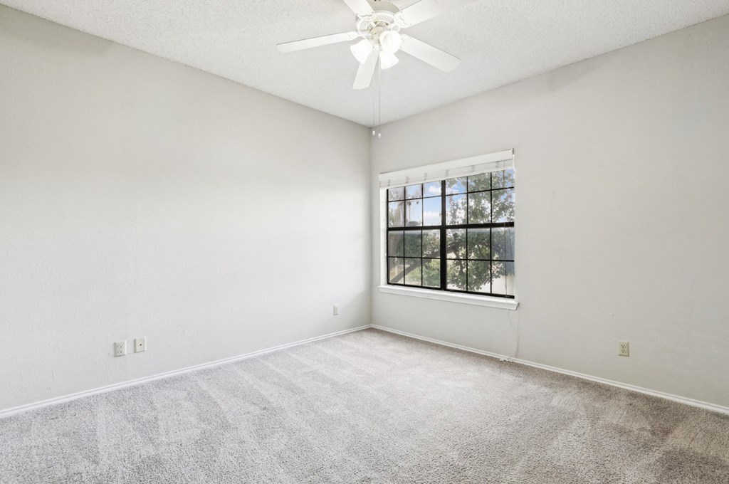 Second bedroom of B1 floor plan with large window and ceiling fan at Jefferson Creek Apartments in Irving, TX.