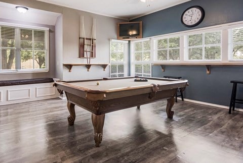 a pool table in a game room with windows and a clock
