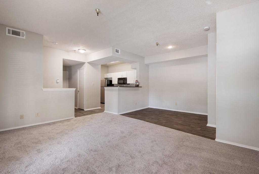 an empty living room with a kitchen in the background