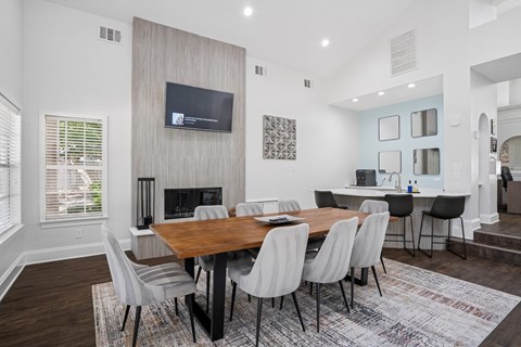 Resident clubhouse area with a wooden table, grey chairs, and a TV at La Costa Apartments in Plano, TX