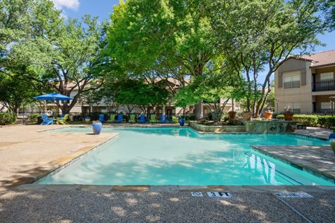A swimming pool surrounded by trees and green and blue chairs at La Costa in Plano, TX.