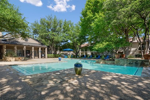 A swimming pool surrounded by trees and the leasing office in the background at La Costa Apartments in Plano, TX