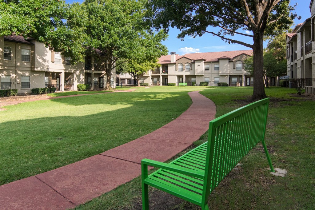 a green park bench sitting on a sidewalk in front of an apartment building