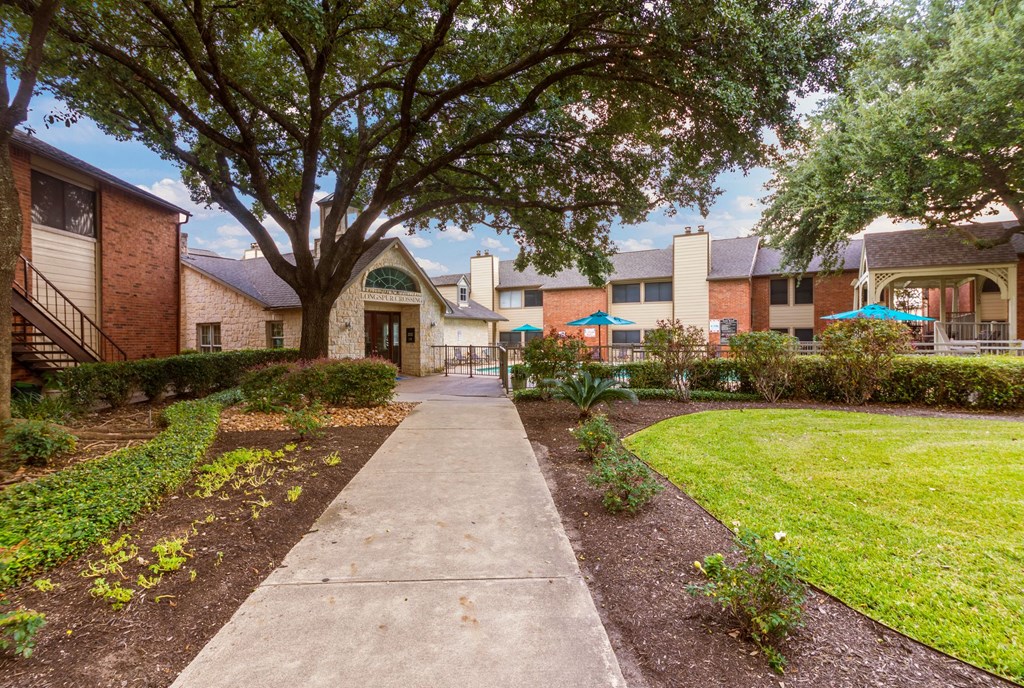 a sidewalk in front of a building with a yard and trees