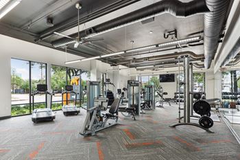 Our gym with a variety of equipment including treadmills, weight machines, and free weights at Muse at Museum District apartments in Houston, TX