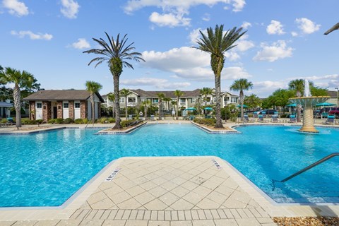 A large swimming pool with fountains is surrounded by palm trees at Oakleaf Plantation Apartments in Jacksonville, FL