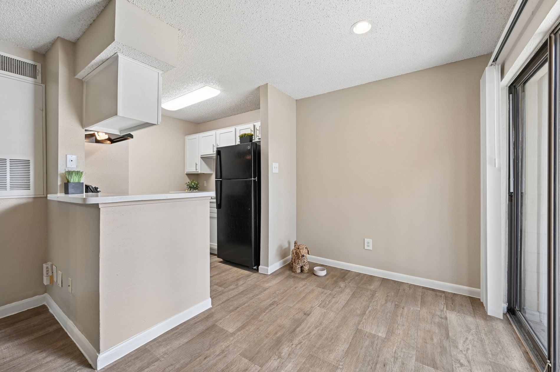 A kitchen area with a black refrigerator and wooden flooring.