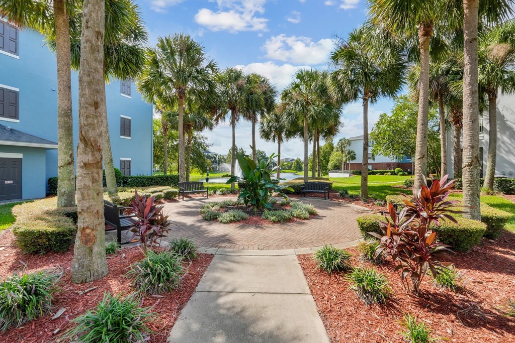 A walkway leads through a landscaped area with palm trees and shrubs at Wynnfield Lakes Apartments in Jacksonville, FL