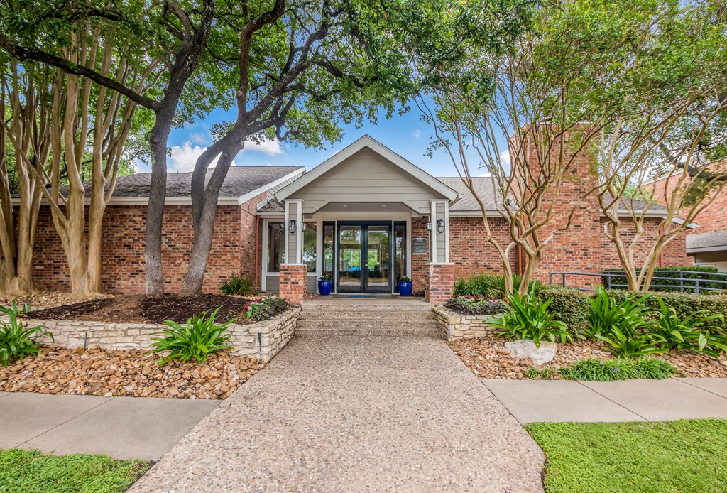 the front of a brick house with a walkway and trees