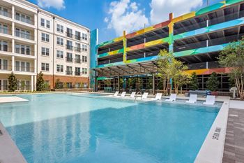 Resort-style swimming pool with in-pool white lounge chairs and parking garage in background at Era Apartments in Denton, TX
