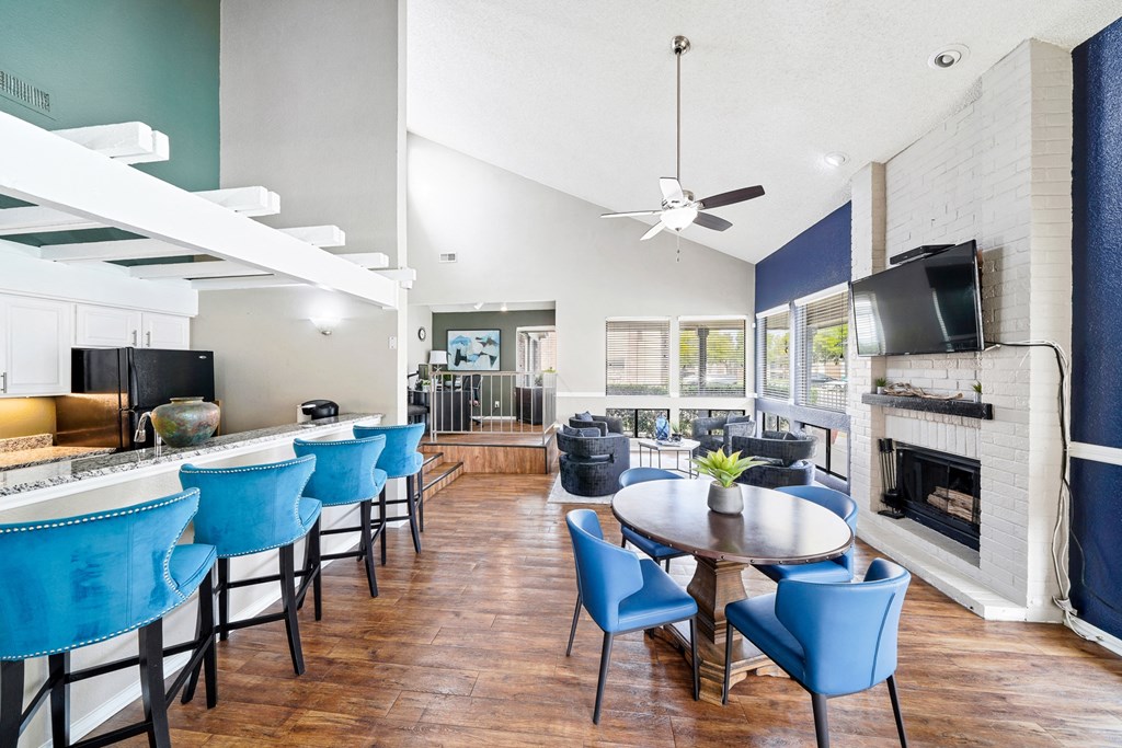 a living room with blue chairs and a kitchen with a table and a television