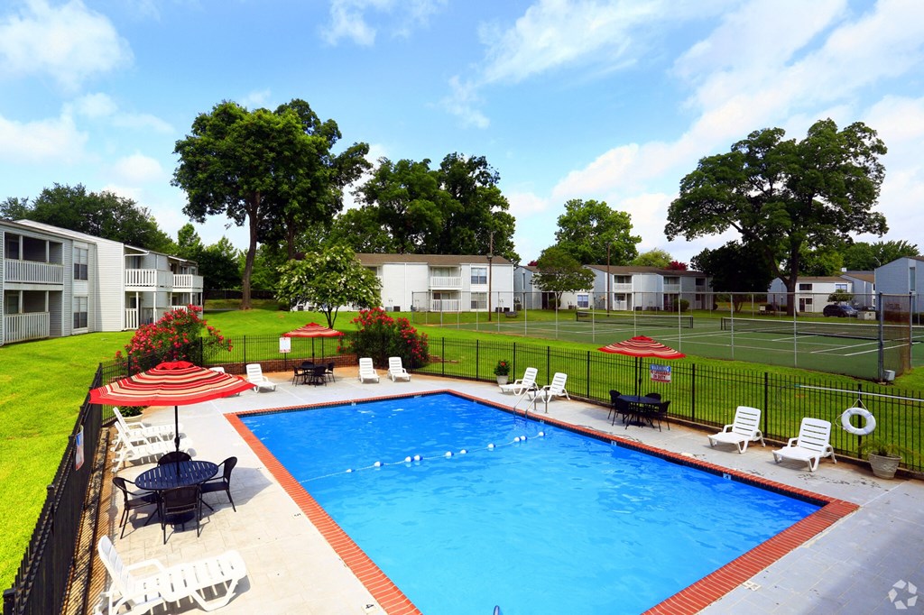 a swimming pool with chairs and umbrellas in front of a yard with houses
