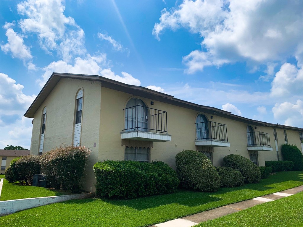 an apartment building with balconies and manicured shrubs and grass