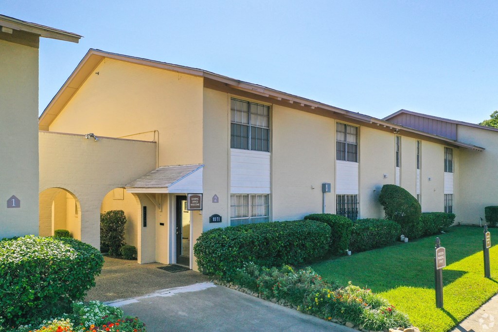 a white building with a lawn and hedges in front of it
