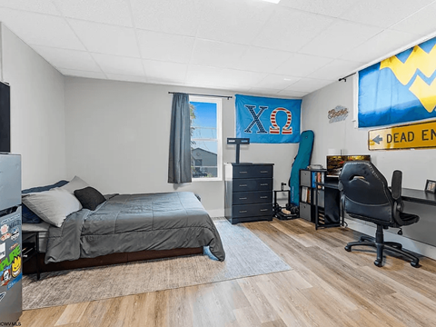 A bedroom with a bed, chair, and a banner with Greek letters on the wall.