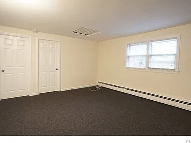A room with a carpeted floor, two doors, and a window.