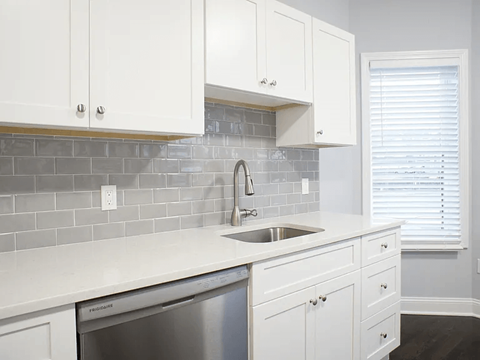 A kitchen with white cabinets and a grey tile backsplash.