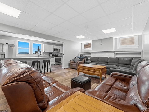 A living room with brown leather furniture and a kitchen area in the background.