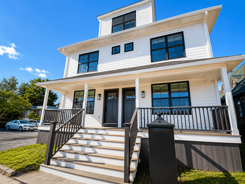 A white two-story house with a black metal railing on the front porch.