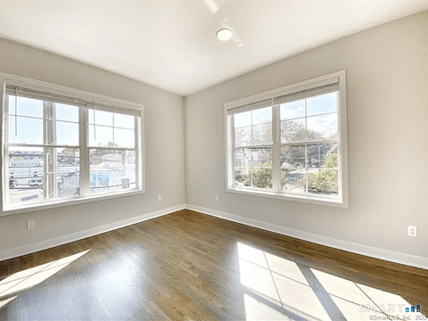 A sunny room with two windows and wooden floors.