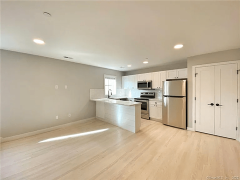 A kitchen with white cabinets and appliances, a large island, and a window.