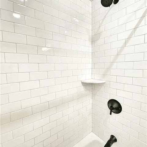 A white tiled shower with a black faucet.