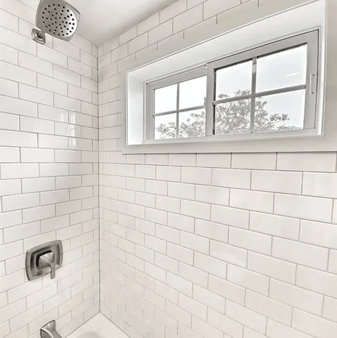 A white tiled bathroom with a window.