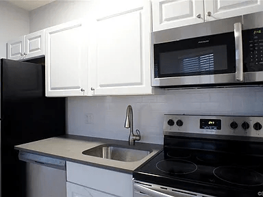 A black refrigerator is in a kitchen with white cabinets.