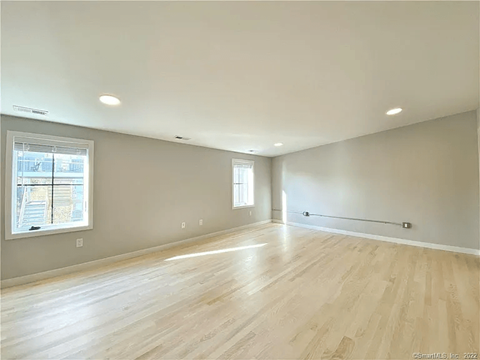 A spacious room with wooden flooring and two windows.