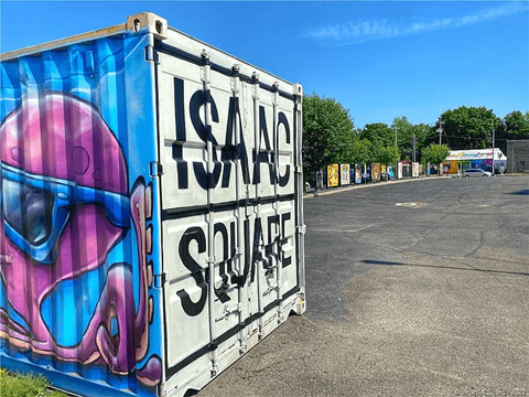 A large container with the words "ISAAC SQUARE" on it is in the foreground of an outdoor parking lot.