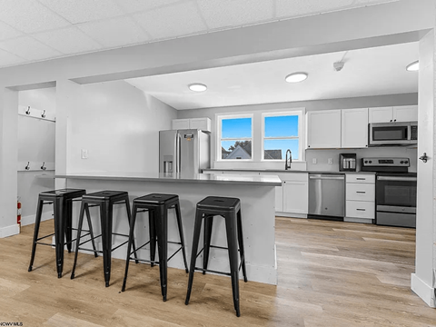 A kitchen with white cabinets and a white island with black bar stools.