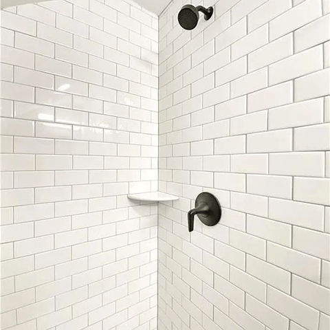 A white tiled shower with a black faucet.