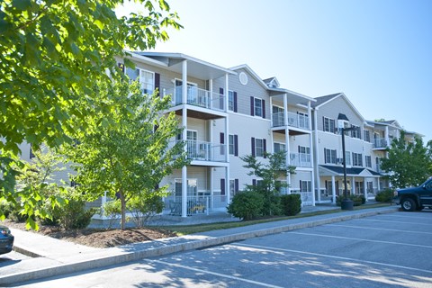A row of white apartment buildings with green trees in the foreground.