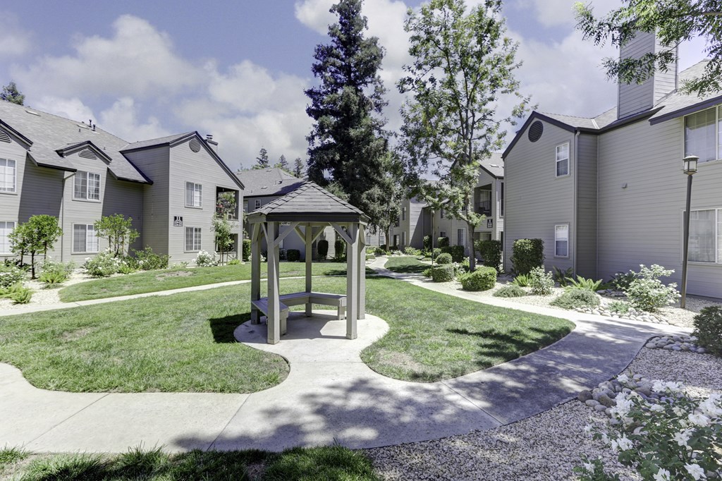 A gazebo sits in the middle of a grassy area in front of apartment buildings.