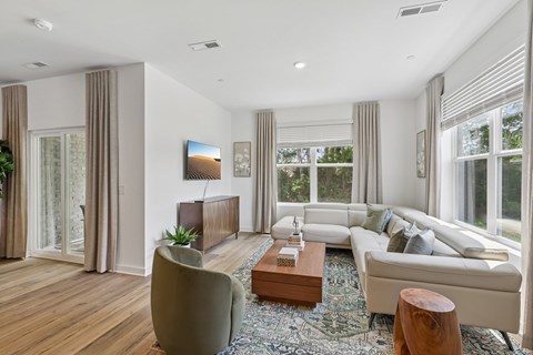 A modern living room with a grey sofa, a wooden coffee table, and a large window with curtains.